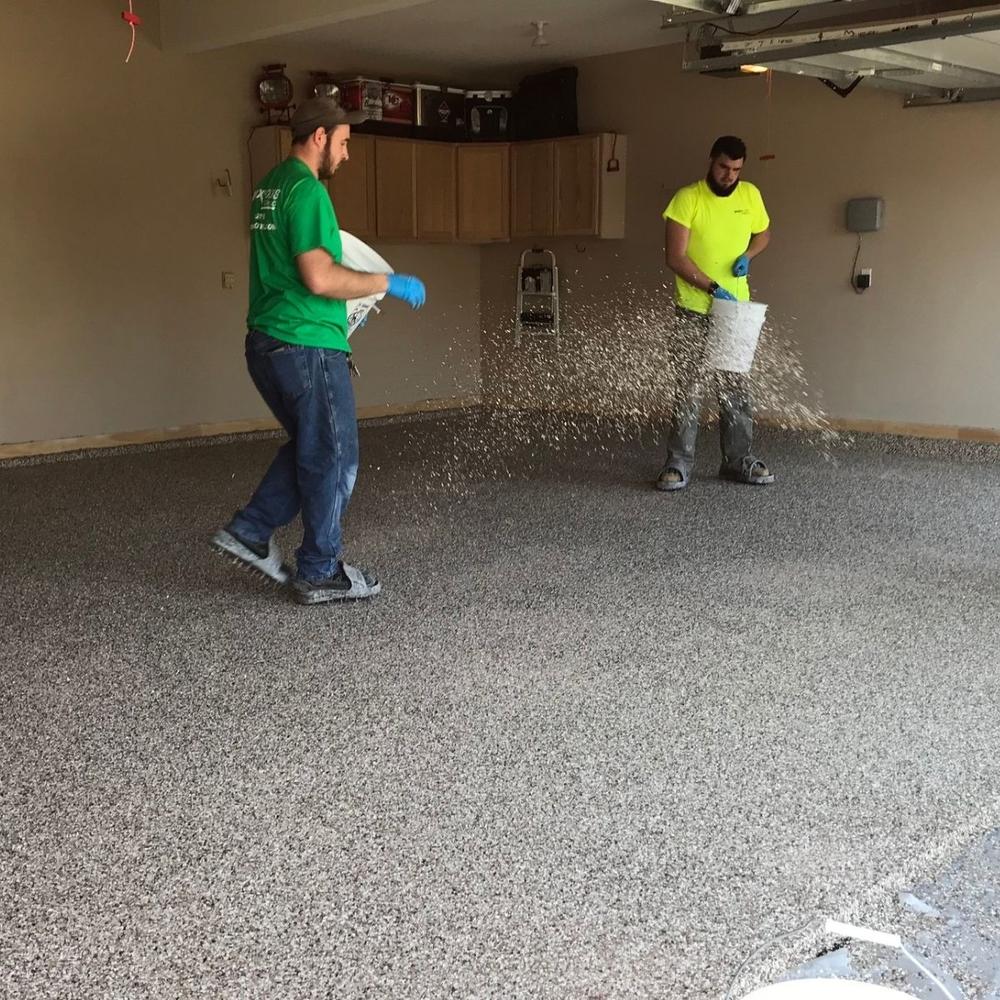 Two crew members hand-broadcasting color flake onto epoxy base coat