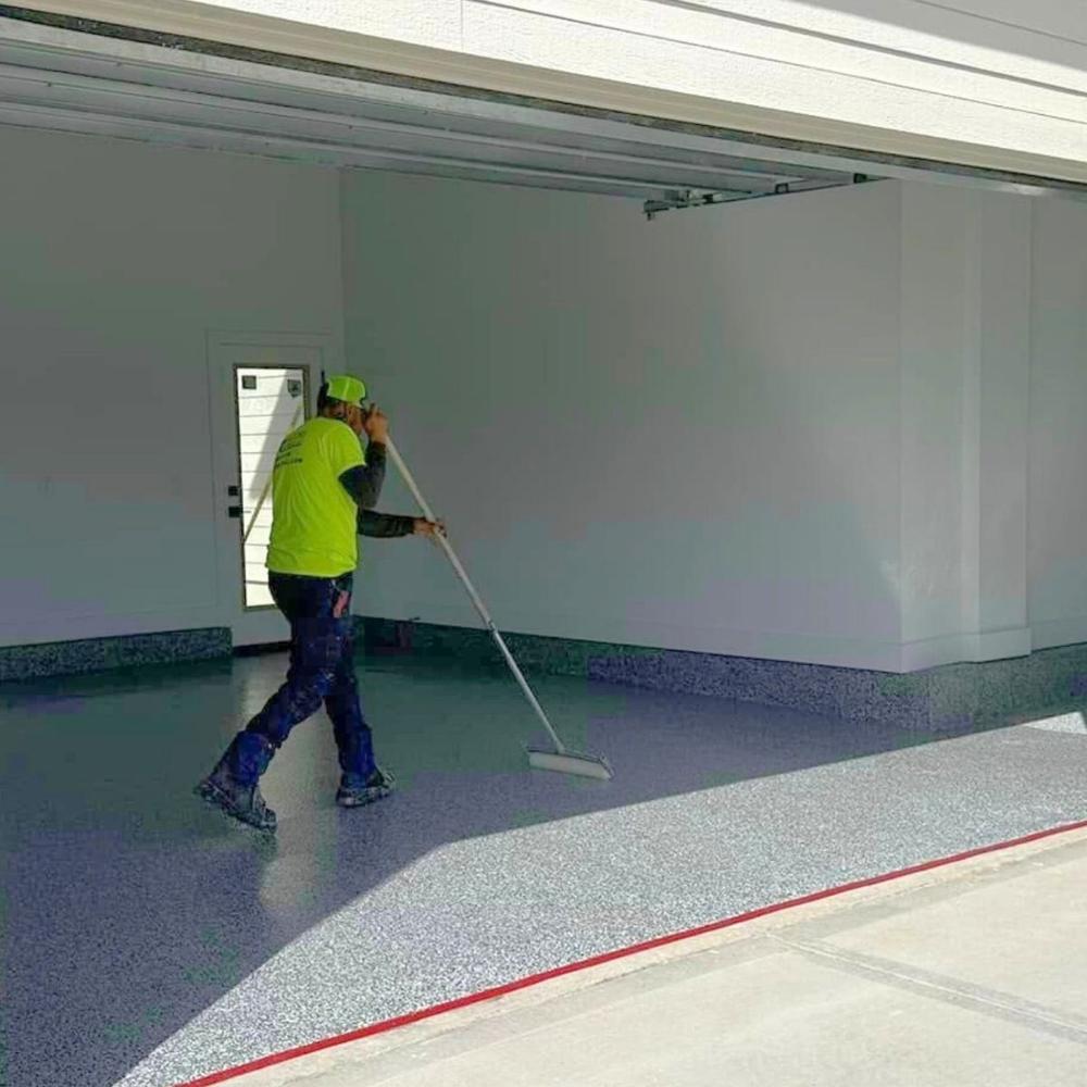 Crew member applying polyaspartic topcoat with roller in garage